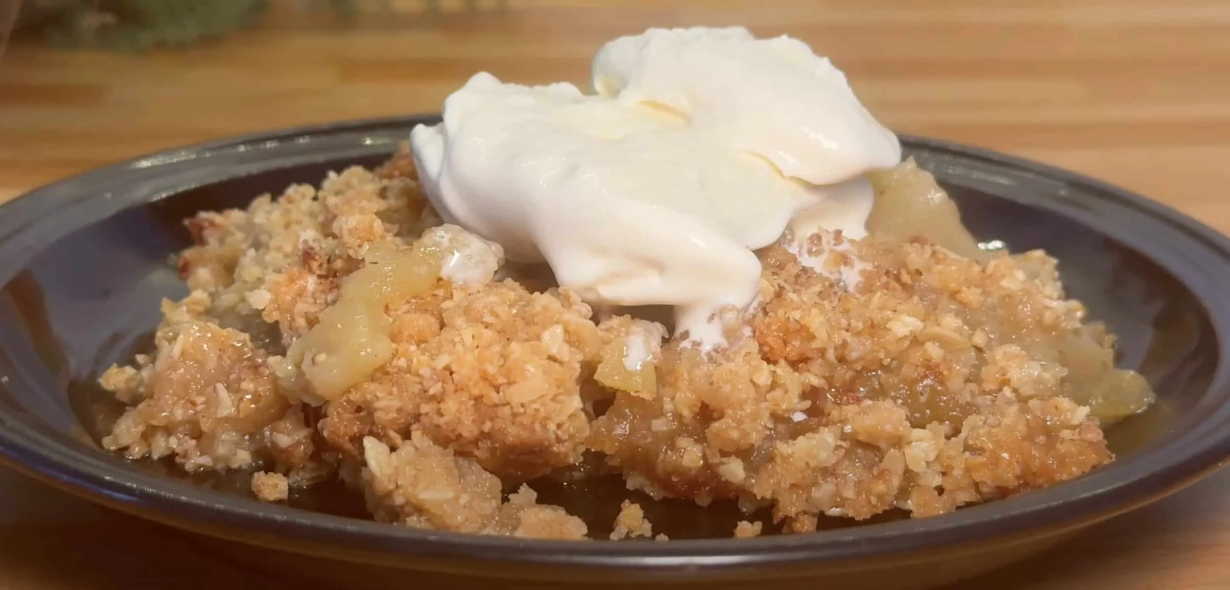 Homemade apple crumble with ice cream on a plate, showcasing a delicious dessert with a crunchy topping.
